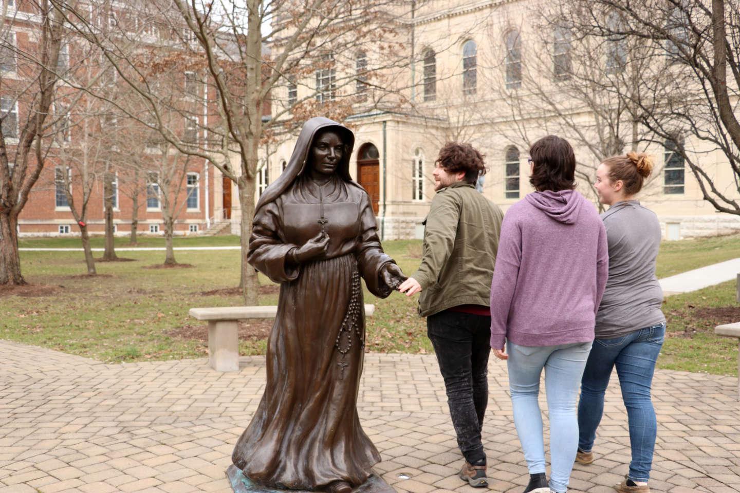 学生 touch the hand of 圣·西奥多·葛兰嬷嬷 as they walk past the statue.